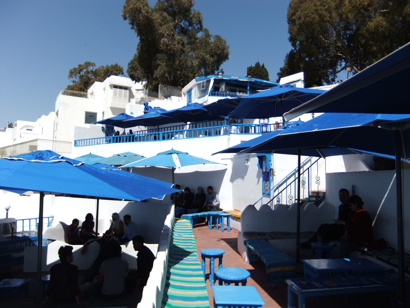 Sunlit cafe terrace with empty tables in front and a few people farther back. Illustrative photograph, not app members or a reservation.