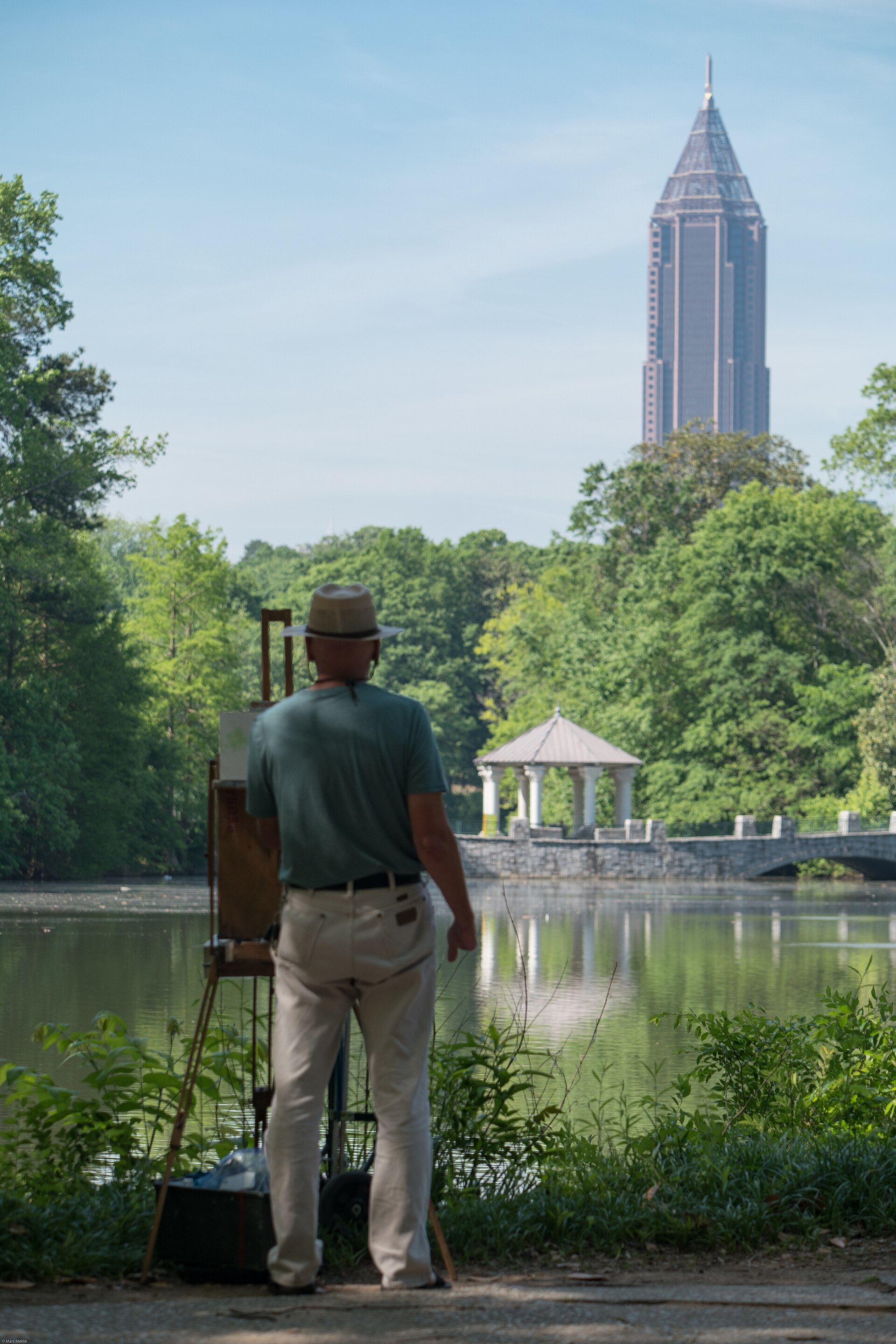 A person seen from the side and back, painting at an easel outdoors beside a lake. Illustrative activity photograph, not a member profile.